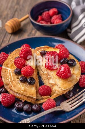 Süße, hausgemachte Pfannkuchen in Scheiben mit Himbeeren und Heidelbeeren auf blauem Teller auf dunklem Holzschreibtisch. Stockfoto