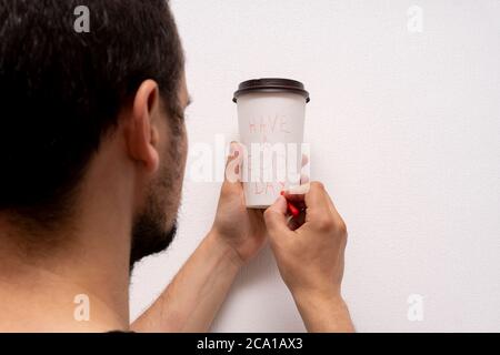 Kaukasischen Mann hält weiße Takeaway Papier Kaffeetasse und schreibt haben einen guten Tag Phrase Stockfoto