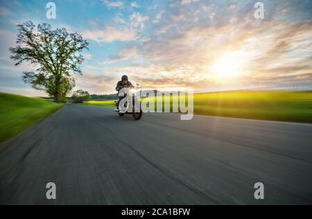 Dunkle Motorradfahrer Reiten High Power Motorrad in der Natur mit schönen Sonnenuntergang Licht. Reisen und Transport. Freiheit beim Motorradfahren Stockfoto