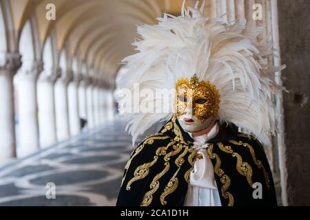 VENEDIG, ITALIEN - 28. JANUAR 2018: Eine Person mit einem typischen schwarzen, weißen und goldenen Kostümkleid und einer goldenen Gesichtsmaske während des Karnevals in Venedig Stockfoto