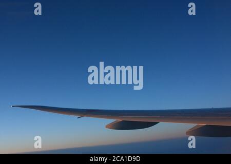 Flugzeugflügel mit Dämmerung und tiefblauem Himmel auf dem Flug nach Japan. Stockfoto