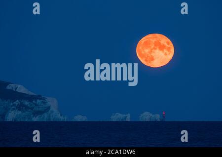 Mudeford, Dorset, Großbritannien. August 2020. Wetter in Großbritannien. Der volle Sturgeon Moon leuchtet orange, als er sich hinter dem Needles Leuchtturm auf der Isle of Wight erhebt, der an einem klaren Sommerabend vom Mudeford Quay in Dorset aus betrachtet wird. Bild: Graham Hunt/Alamy Live News Stockfoto