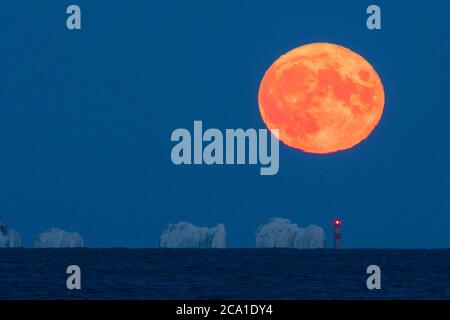 Mudeford, Dorset, Großbritannien. August 2020. Wetter in Großbritannien. Der volle Sturgeon Moon leuchtet orange, als er sich hinter dem Needles Leuchtturm auf der Isle of Wight erhebt, der an einem klaren Sommerabend vom Mudeford Quay in Dorset aus betrachtet wird. Bild: Graham Hunt/Alamy Live News Stockfoto