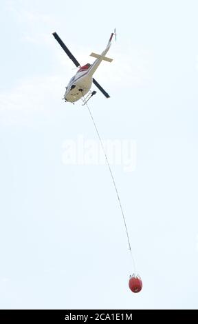 Sidney, British Columbia, Kanada 03. Aug. 2020 - EIN Hubschrauber von VIH Helicopters, der an einem Wassereimer (unten) befestigt ist, hebt sich vom Shell Aerocenter am Victoria International Airport ab, um Waldbrände zu bekämpfen. Die jüngste heiße Trockenheit hat in der gesamten Provinz zu einem starken Anstieg der Waldbrände geführt. Der Hubschrauber taucht den Eimer in einen nahe gelegenen See und lässt ihn dann über die Feuerzone fallen. Don Denton/Alamy Live News Stockfoto