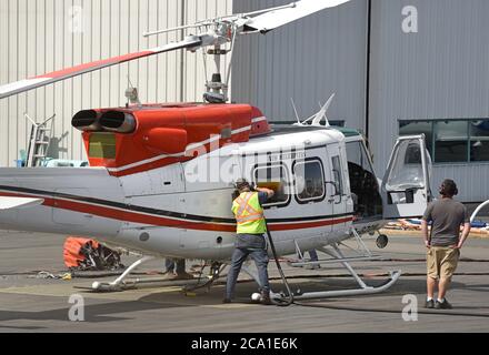 Sidney, British Columbia, Kanada 03. Aug. 2020 - EIN Hubschrauber von VIH Helicopters, der an einem Wassereimer (unten links) befestigt ist, wird vor dem Start vom Shell Aerocenter am Victoria International Airport aufgetankt, um Waldbrände zu bekämpfen. Die jüngste heiße Trockenheit hat in der gesamten Provinz zu einem starken Anstieg der Waldbrände geführt. Der Hubschrauber taucht den Eimer in einen nahe gelegenen See und lässt ihn dann über die Feuerzone fallen. Don Denton/Alamy Live News Stockfoto