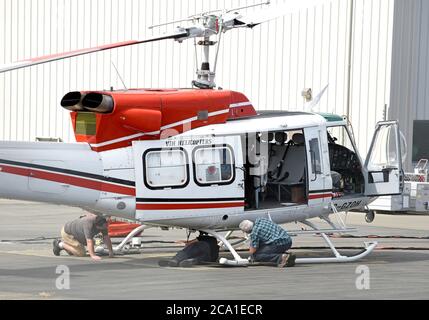 Sidney, British Columbia, Kanada 03. Aug. 2020 - EIN VIH Helicopters Hubschrauber, der an einem Wassereimer (hinter dem Mann unten links) befestigt ist, wird von der Flug- und Bodencrew überprüft, bevor er vom Shell Aerocenter am Victoria International Airport abfliegt, um Waldbrände zu bekämpfen. Die jüngste heiße Trockenheit hat in der gesamten Provinz zu einem starken Anstieg der Waldbrände geführt. Der Hubschrauber taucht den Eimer in einen nahe gelegenen See und lässt ihn dann über die Feuerzone fallen. Don Denton/Alamy Live News Stockfoto