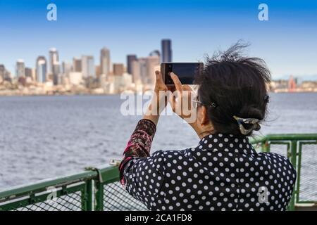 SEATTLE, STAAT WASHINGTON, USA - JUNI 2018: Person, die ein Bild der Skyline der Stadt mit einem Kameratelefon vom Deck einer Passagierfähre macht. Stockfoto