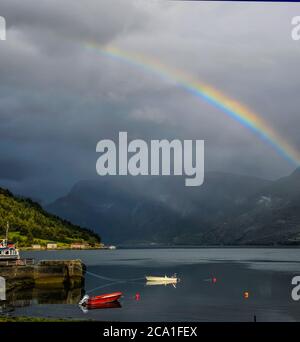 Ein Regenbogen über Booten in Solvorn, Norwegen. Solvorn liegt am östlichsten Punkt des Sognefjord Fjords in Norwegen. Stockfoto