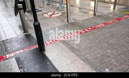 Rote Linie auf dem Bürgersteig mit RAUCHVERBOT Text, Schild in der Nähe auch Fußgänger, die sie betreten Nichtraucher-Bereich. Stockfoto