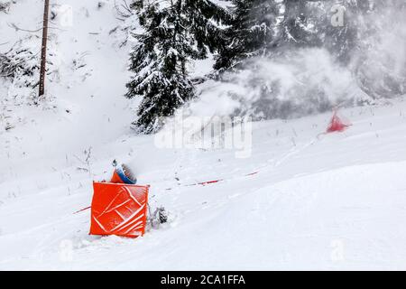 Schneekanone Spritzen künstliche Eiskristalle über Skipiste, Bäume im Hintergrund Stockfoto