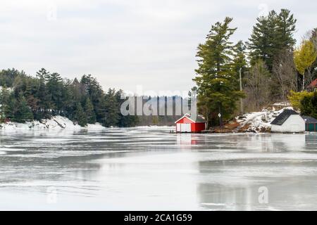 See Rosseau mit Bootshäusern entlang der Küste während eines Wintertauens, Rosseau, Ontario, Kanada Stockfoto