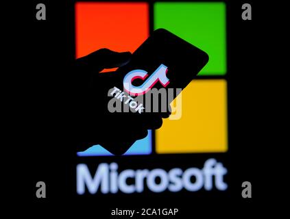 Stone / UK - 3. August 2020: TikTok App auf der Silhouette des mobilen Hold in der Hand. Microsoft-Logo auf verschwommenem Display hinter gesehen. Selektiver Fokus. Stockfoto