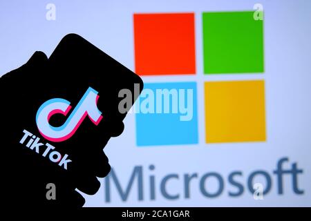 Stone / UK - 3. August 2020: TikTok App auf der Silhouette des mobilen Hold in der Hand. Microsoft-Logo auf verschwommenem Display hinter gesehen. Selektiver Fokus. Echt Stockfoto