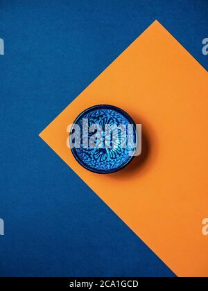 Leere blaue Keramikschale auf orangefarbenem und blauem Hintergrund. Overhead-Aufnahme mit Kopierplatz. Stockfoto