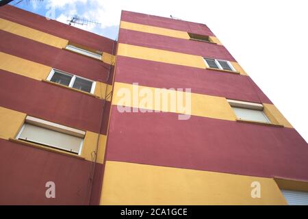 Blick auf ein Hochhaus mit Fenstern zur Straße, deren Fassade in roten und gelben Streifen gestrichen ist Stockfoto