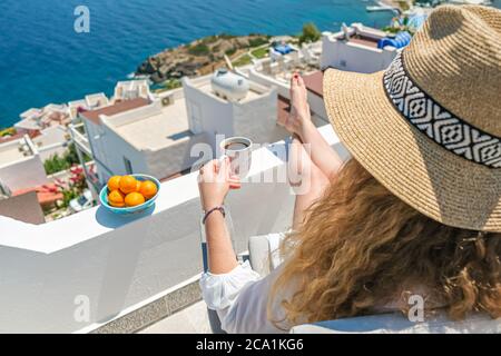 Schöne junge Frau Strohhut und Kaffeetasse sitzen auf der weißen Terrasse Balkon des Hauses oder Hotel mit Meerblick Stockfoto