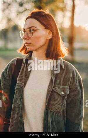 Nahaufnahme Outdoor-Porträt von stilvollen schönen kaukasischen junge Frau mit kurzen Brünette Haare tragen Jeans-Hemd und Brille. Sommer sonnig Abend par Stockfoto