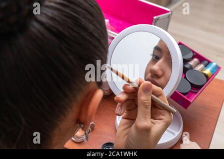 Teenager-Mädchen durch einen kleinen Spiegel suchen, während auf Make-up in ihrem Wohnzimmer setzen Stockfoto