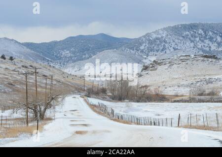 Ländliche Colorado Schneelandschaft mit Rocky Mountain Ausläufern, schneebedeckte Straße, Telefonumfragen und Zäune Stockfoto