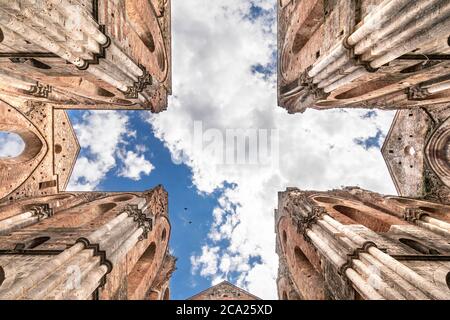 Symmetrische Ansicht des kreuzförmigen Querschiffs einer alten verlassenen Kirche von unten gesehen, unter einem blauen Sommerhimmel mit Wolken Stockfoto