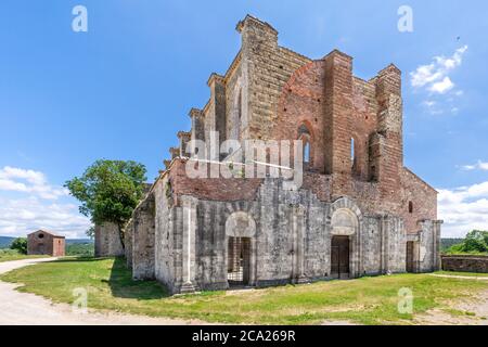 Weitwinkelansicht der Außenseite einer alten und verlassenen tuscanischen gotischen Kathedrale, mit einem Baum wächst auf seiner Seite, unter einem blauen Sommerhimmel Stockfoto