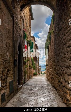 Eine ikonische schmale Gasse in der toskanischen Stadt Pienza, mit italienischen Fahnen haning aus den Fenstern und führt zu einem Aussichtspunkt auf die Landschaft Stockfoto