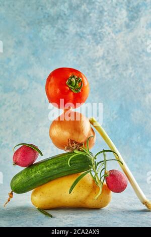 Eine Gourmet-Food-Komposition mit buntem Gemüse auf blauem Hintergrund, für eine lustige Gastronomie und vegetarisches Rezept. Gleichgewicht schwimmende Lebensmittel Balanc Stockfoto