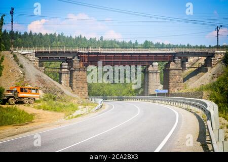 Alte Eisenbahnbrücke über die Autobahn und den Fluss Urschumka. Südural, Russland. Stockfoto