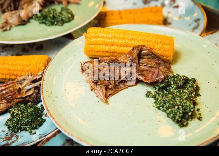 Saftiges, frisch zubereitetes Fleisch wird auf dem Maiskolben und der grünen Soße serviert. Das Essen liegt auf einem runden Teller. Bereit zum servieren. Stockfoto