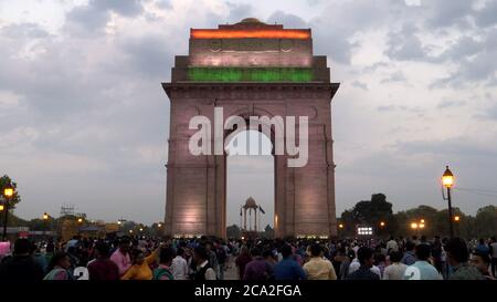 DELHI, INDIEN - 14. MÄRZ 2019: Menschenmengen um das tor von indien, das in der Abenddämmerung mit einer Flagge beleuchtet wird Stockfoto