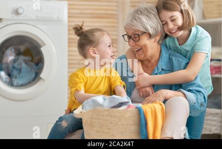 Glückliche Oma und Kinder Mädchen kleine Helfer haben Spaß und lächeln, während Wäsche zu Hause. Stockfoto