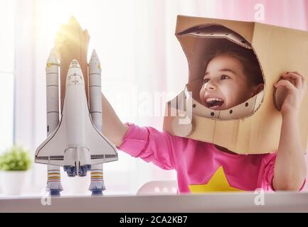 Mädchen in einem Astronaut Kostüm mit Spielzeug Rakete spielen und träumen von einem Raumfahrer zu werden. Portrait von lustigen Kind in der Nähe von Fenstern. Stockfoto