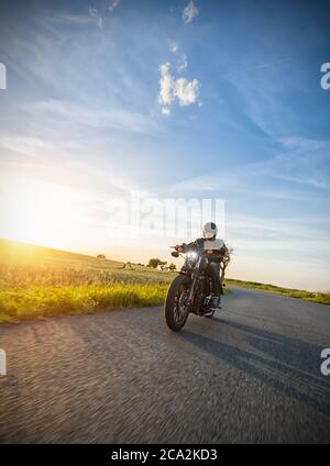 Dunkle Motorradfahrer Reiten High Power Motorrad in der Natur mit schönen Sonnenuntergang Licht. Reisen und Transport. Freiheit beim Motorradfahren Stockfoto