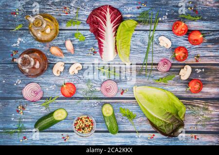 Salatzutaten auf einem farbigen Holztisch mit Tomaten, Gurken, Rucola, Salzkörnern, Schnittlauch, Pfefferkörnern, Dill, Petersilie, Pilzen, Rot Stockfoto