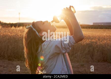 Mädchen trinkt Wasser aus einer Flasche bei Sonnenuntergang Stockfoto