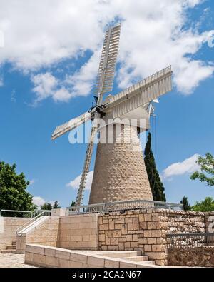 Antike montefiore Windmühle in jerusalem in israel sitzt auf einer Steinmauer über einem Park mit einem teilweise bewölkten Himmel im Hintergrund Stockfoto