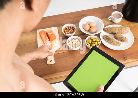 High-Winkel-Rückansicht von muskulösen Mann ohne Kleidung halten Tablette zeigt gesunde Ernährung Menü auf dem Tisch nach vorne auf isolierten Hintergrund Stockfoto