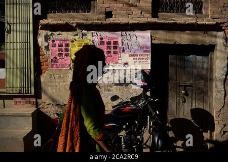 Eine Frau, die auf einer Wohnallee in der Altstadt von Bhaktapur vor einem gemauerten Gebäude mit Werbeplakaten an der Wand läuft. Stockfoto