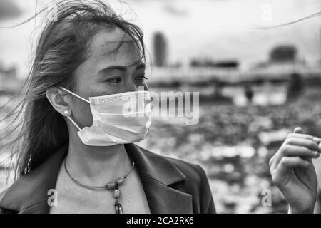 Schöne asiatische Frau im Freien trägt Gesichtsmaske. Stockfoto