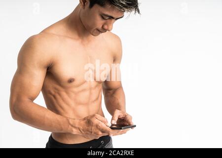 Zugeschnittenes Bild von asiatischen jungen Mann mit muskulösen Körper halten Ein Smartphone mit zwei Hand Tippstand nach vorne und Betrachten Sie ein Telefon auf isoliertem Hintergrund Stockfoto