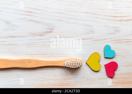 Bambuszahnbürste und drei bunte Holzherzen auf Holzhintergrund. Biologisch abbaubare Bambuszahnbürste mit Kopierplatz. Naturprodukt für Bad. Null Stockfoto