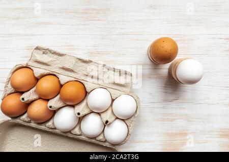 Kartonbehälter mit braunen und weißen Eiern und gekochten Eiern in Haltern auf Holztisch. Hühnereier in recyceltem Karton auf Holzhintergrund. Free-r Stockfoto