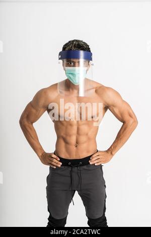 asian Mann zeigen muskulösen Körper tragen eine Maske und Gesichtsschutz mit zwei Händen auf Taille stehen nach vorne und Blick auf die Kamera auf isolierten Hintergrund Stockfoto