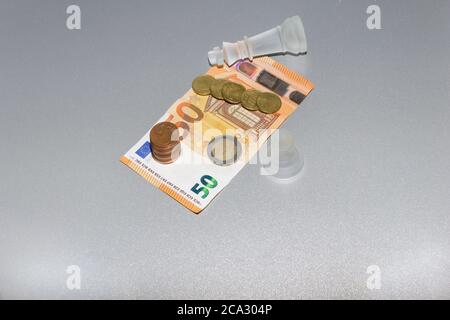 Euro-Münzen und 50 Euro Banknote, mit Schachkönig und Spielfiguren auf isoliertem grauen Hintergrund. Business bankrott, sparen und Finanzen Konzept. Stockfoto