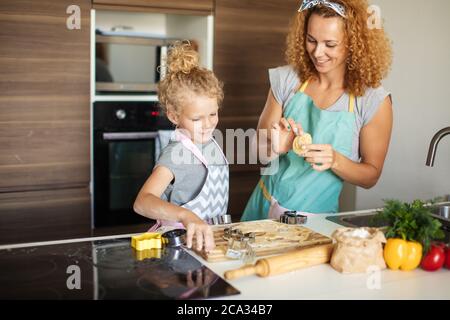 Krauses blondes Haar Mutter und ihre entzückende Tochter mit lockigen blonden Haaren Schneiden Formen aus Teig für Cookies in der Küche. Kleines Mädchen mit m Stockfoto