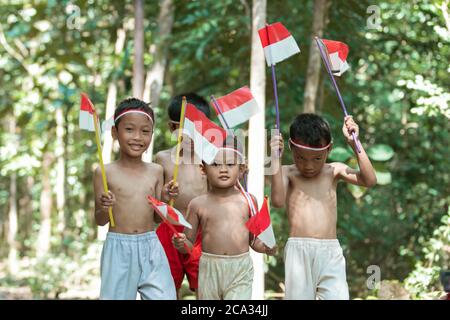 Gruppe von Kindern gehen mit kleinen roten und weißen Fahne zusammen mit vielen Bäumen im Hintergrund Stockfoto
