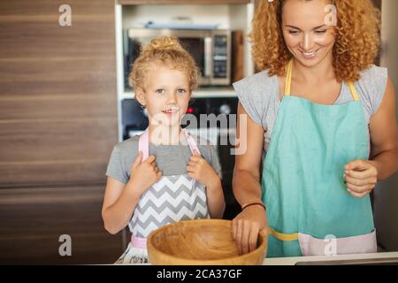 Zwei Blondinen kochen in der Küche. Kaukasische hübsche junge Frau und ihre kleine süße Tochter kochen in der Küche, Draufsicht. Stockfoto