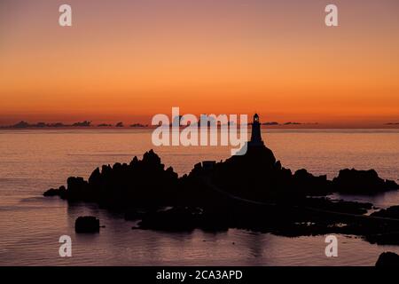 Sonnenuntergang in Corbiere auf der Insel Jersey, mit den Felsen und dem Leuchtturm vor dem dramatischen Himmel Stockfoto