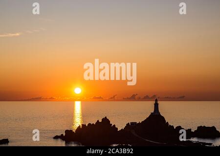 Sonnenuntergang in Corbiere auf der Insel Jersey, mit den Felsen und dem Leuchtturm vor dem dramatischen Himmel Stockfoto