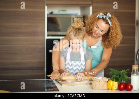 Junge kleine Mädchen, Mama s Helfer Unterstützung Mutter bei der Vorbereitung Eastern Brot für den Urlaub, Ausrollen des Teiges mit Mutter s Hände in der Nähe. Stockfoto